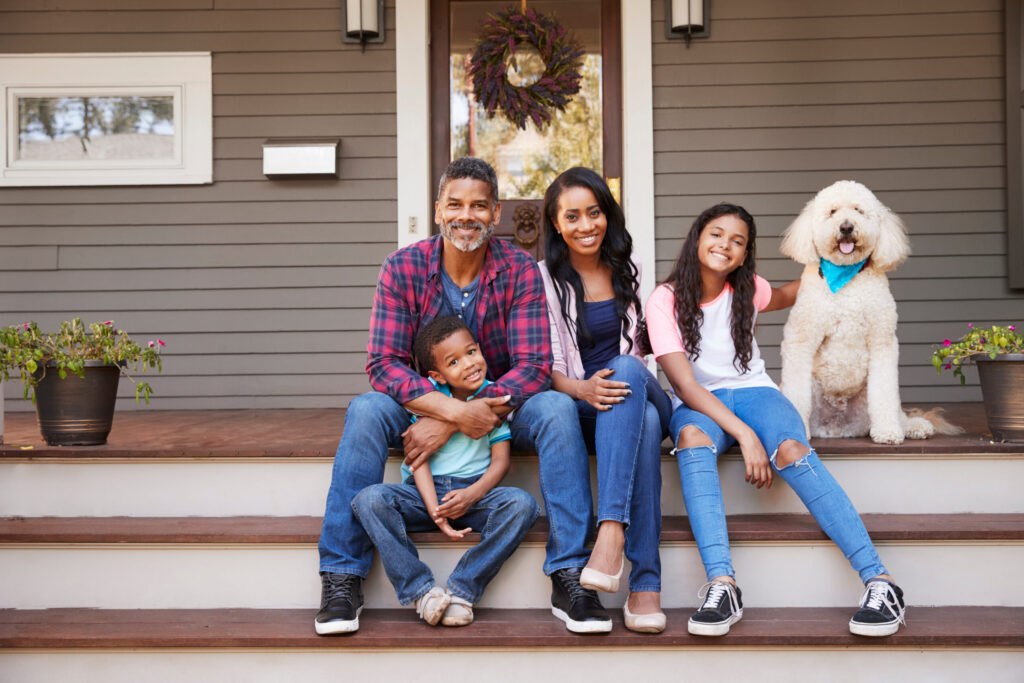 Family With Children And Pet Dog Sit On Steps Of Home